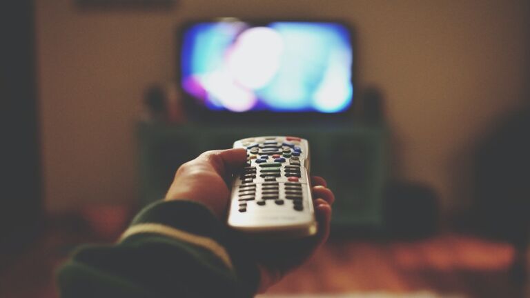 Cropped Of Person Holding Remote Control Against Television Set At Home