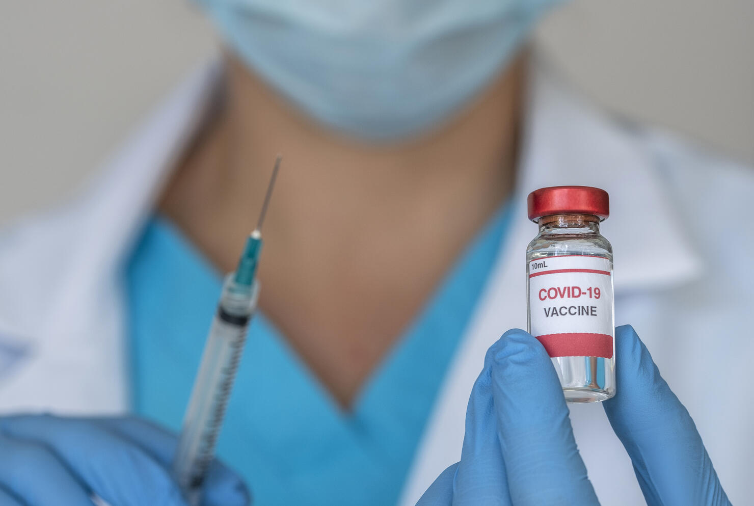 Close-up of doctors hands holding Covid-19 vaccine and syringe