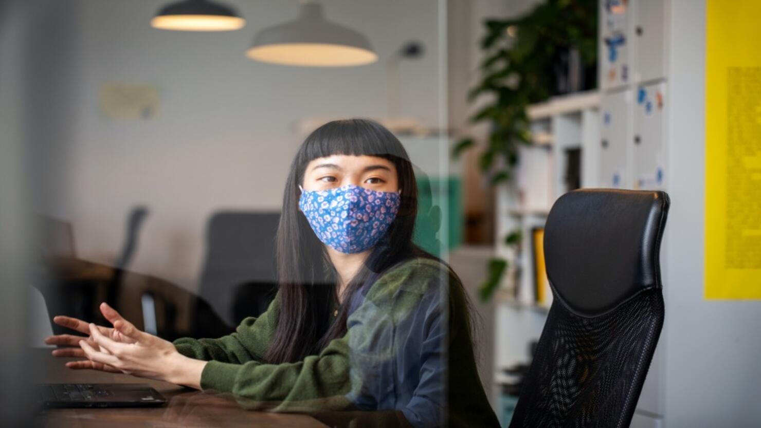 Businesswoman discussing work with colleague through glass shield on desk