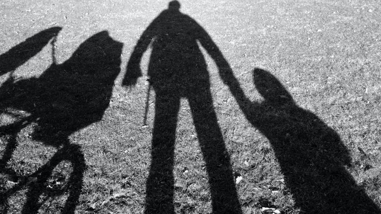 Shadows of person holding hands with a baby and a stroller