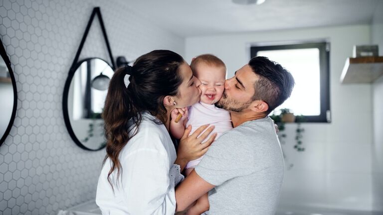 Portrait of young couple with toddler girl in the morning indoors in bathroom at home, kissing.