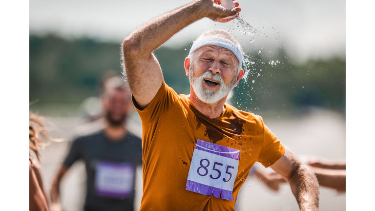 Exhausted mature runner pouring fresh water on his head during a marathon race.