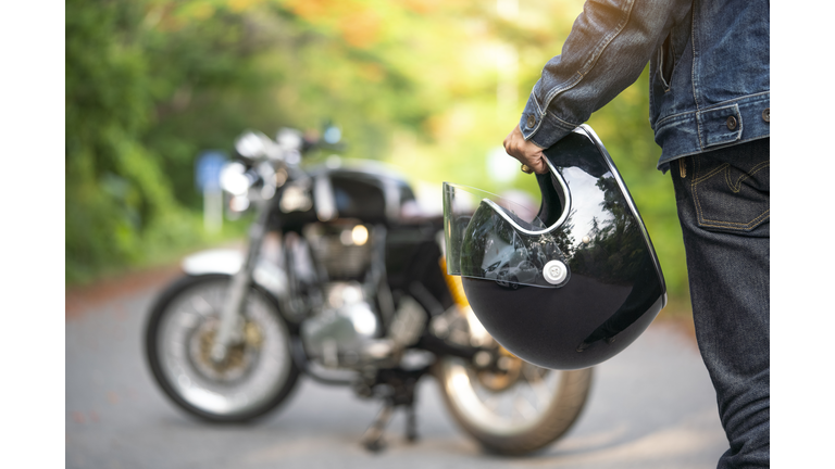 Handsome man in jean is holding a helmet and vintage motorcycle blur background