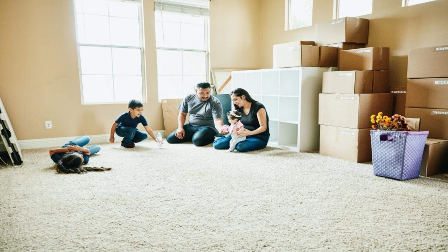 Family sitting on floor of living room of new home during move in day