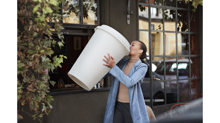 Woman drinking coffee from large disposable cup at take away counter of cafe