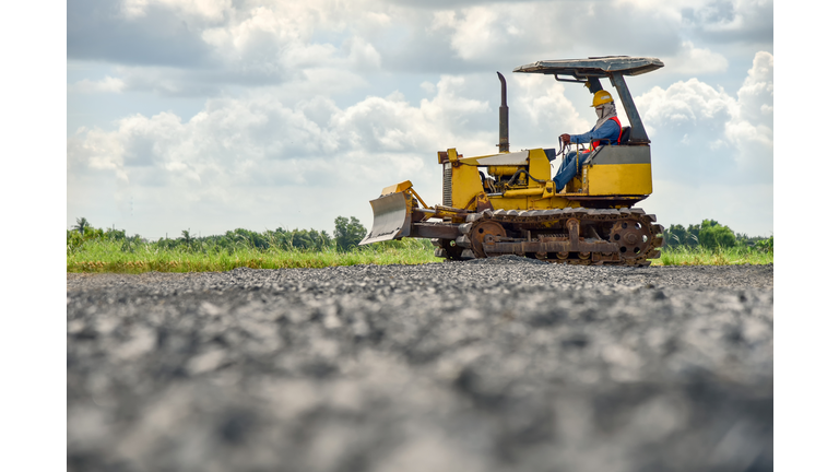 Construction worker in safety uniform driving grader tractor or construction machine move the soil in construction site and beautiful sky background