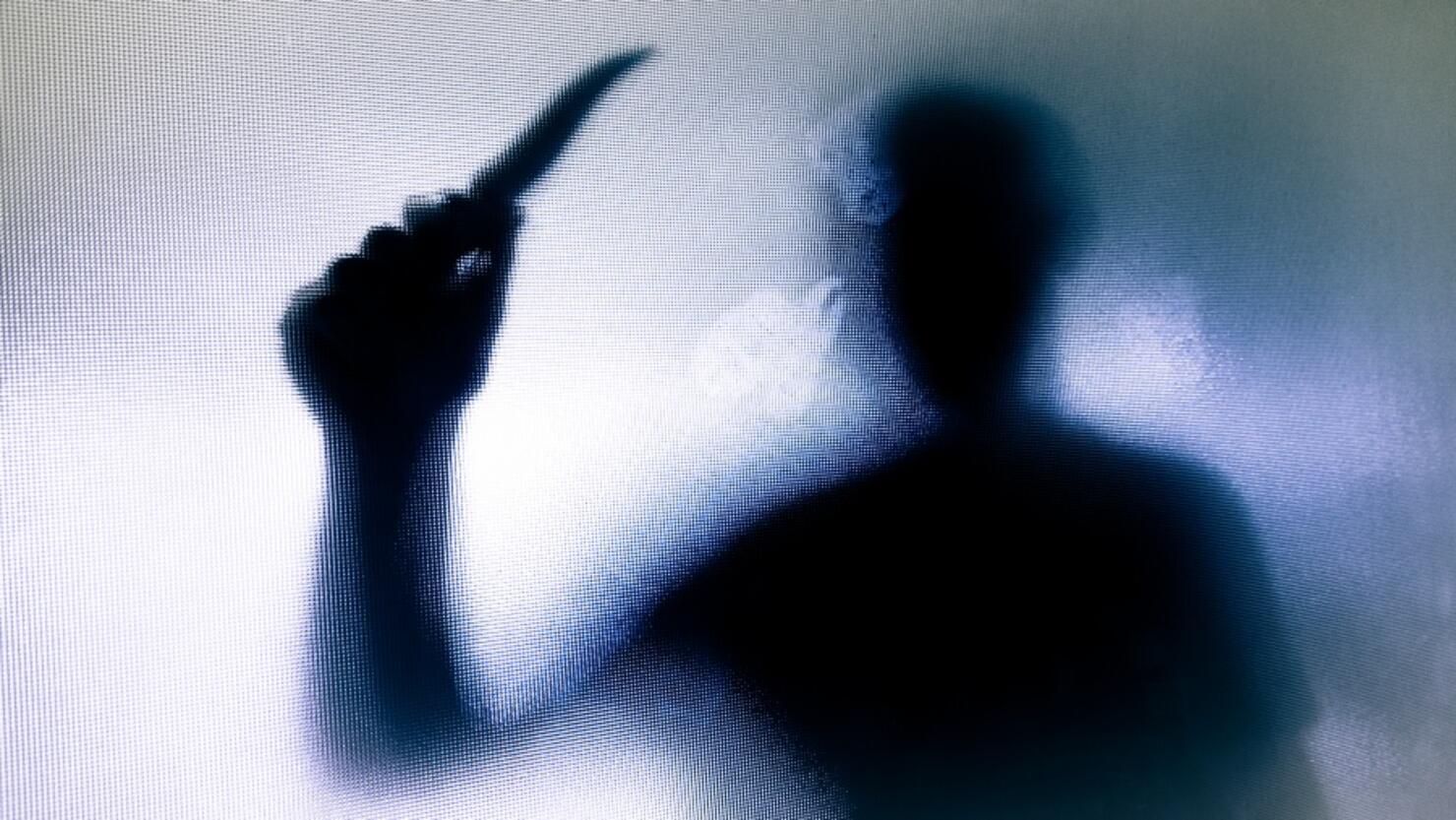 Violent threatening silhouette of man wielding a knife behind frosted glass window