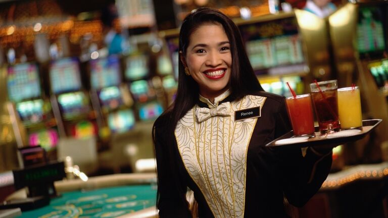 Waitress carrying tray of cocktails in casino, smiling, portrait