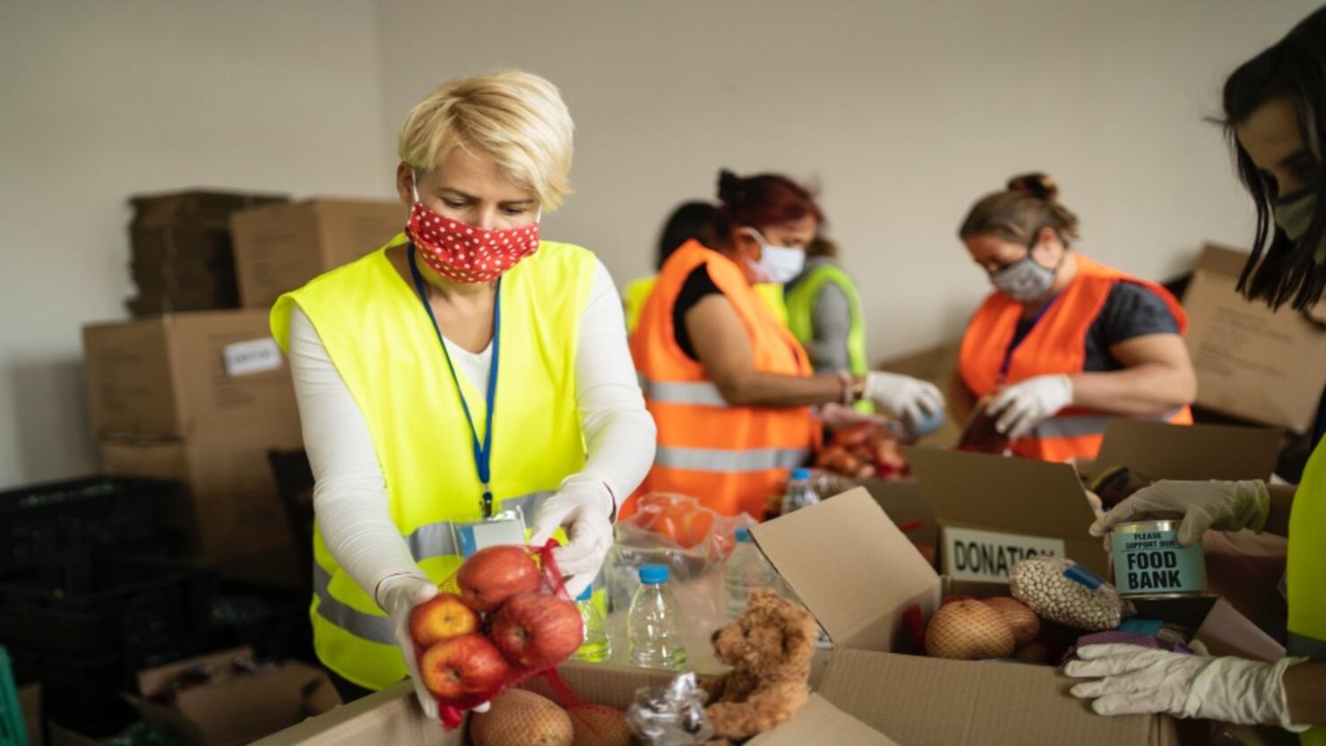 Woman with protective face mask helping collecting food in a homeless shelter