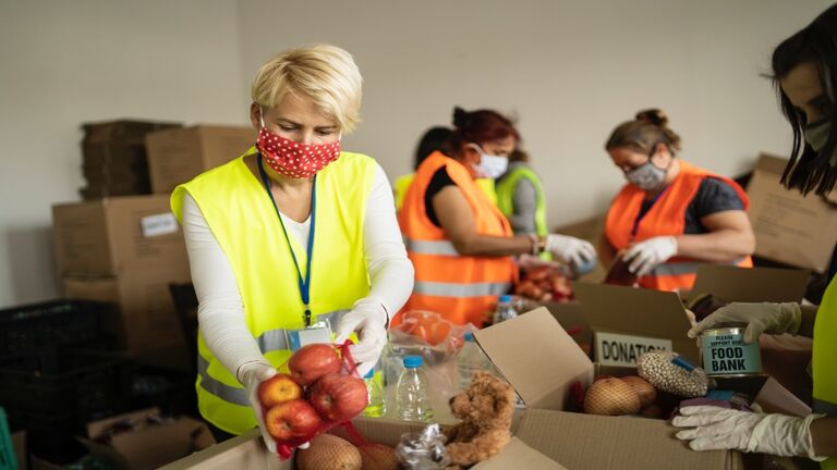 Woman with protective face mask helping collecting food in a homeless shelter