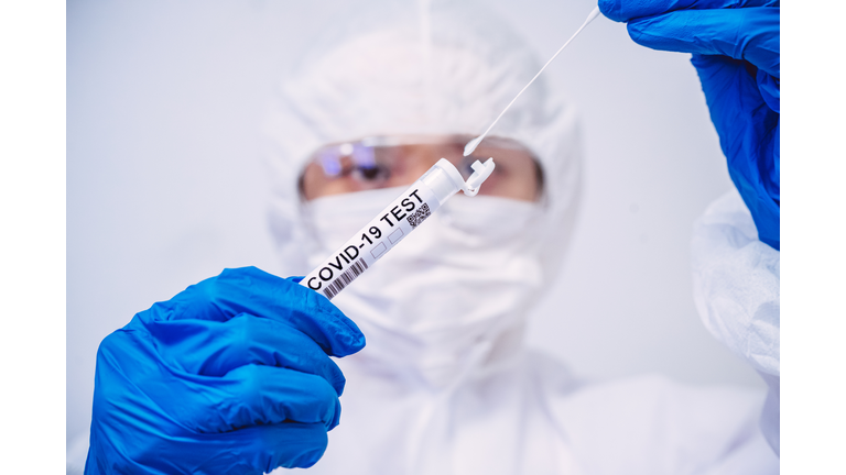 Doctor in protective gloves & workwear holding open test tube and taking out sampling swab for novel Covid-19 test