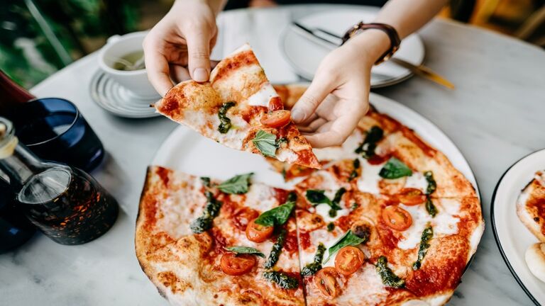 Overhead view of woman's hand getting a slice of freshly made pizza and enjoying her meal in an Italian restaurant