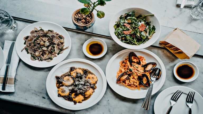 Flat lay of meal for two people with fresh green salad, appetizer, seafood linguine and beef ravioli freshly served on dining table in a restaurant