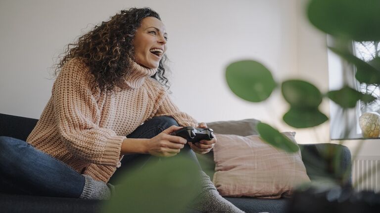 Woman sitting on couch, having fun, playing with a gaming console