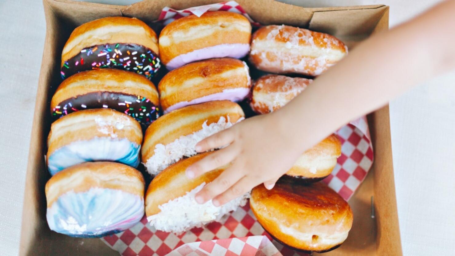 Cropped Hand Touching Donuts In Box