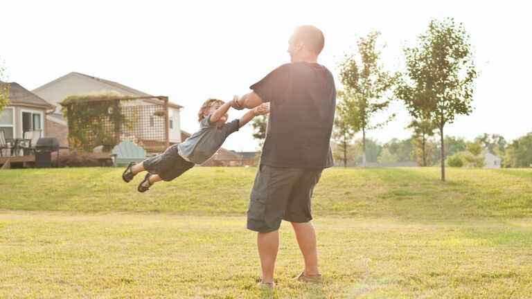 Father swinging young boy outside on grass
