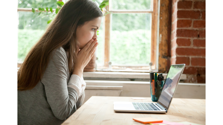 Shocked young woman looking at laptop screen at work desk.