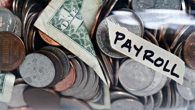 Close-up of coins and banknotes in jar labeled Payroll