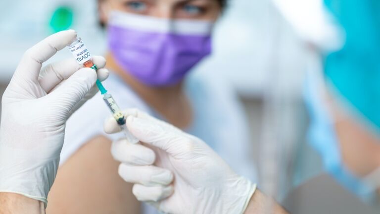 Doctor's hands in surgical gloves preparing COVID-19 vaccine for female patient