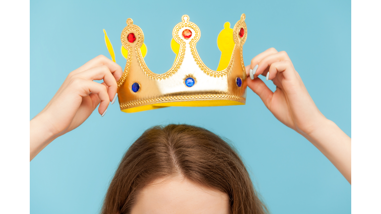 Closeup of woman putting on head golden crown, concept of awards ceremony, privileged status, superior position