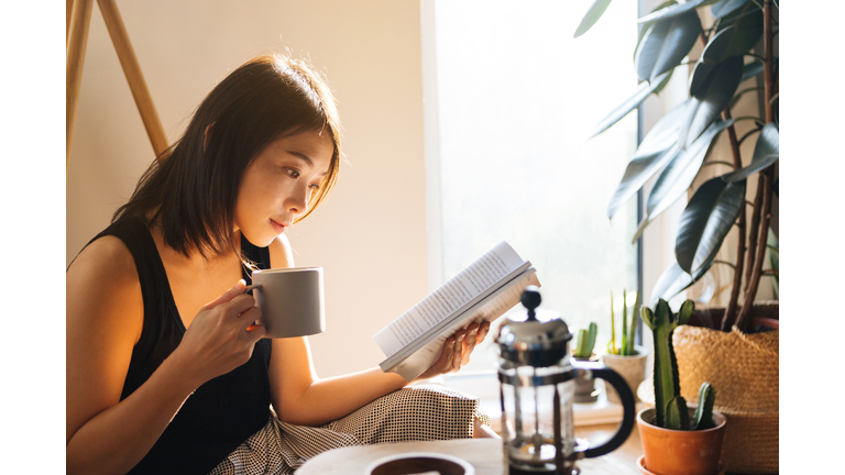 Young Woman Reading Book While Drinking Coffee