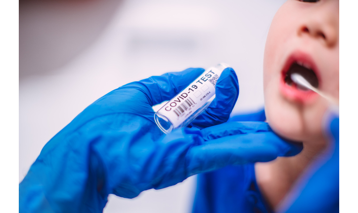 Doctor’s hands in protection gloves putting COVID-19 test swab into kid’s mouth