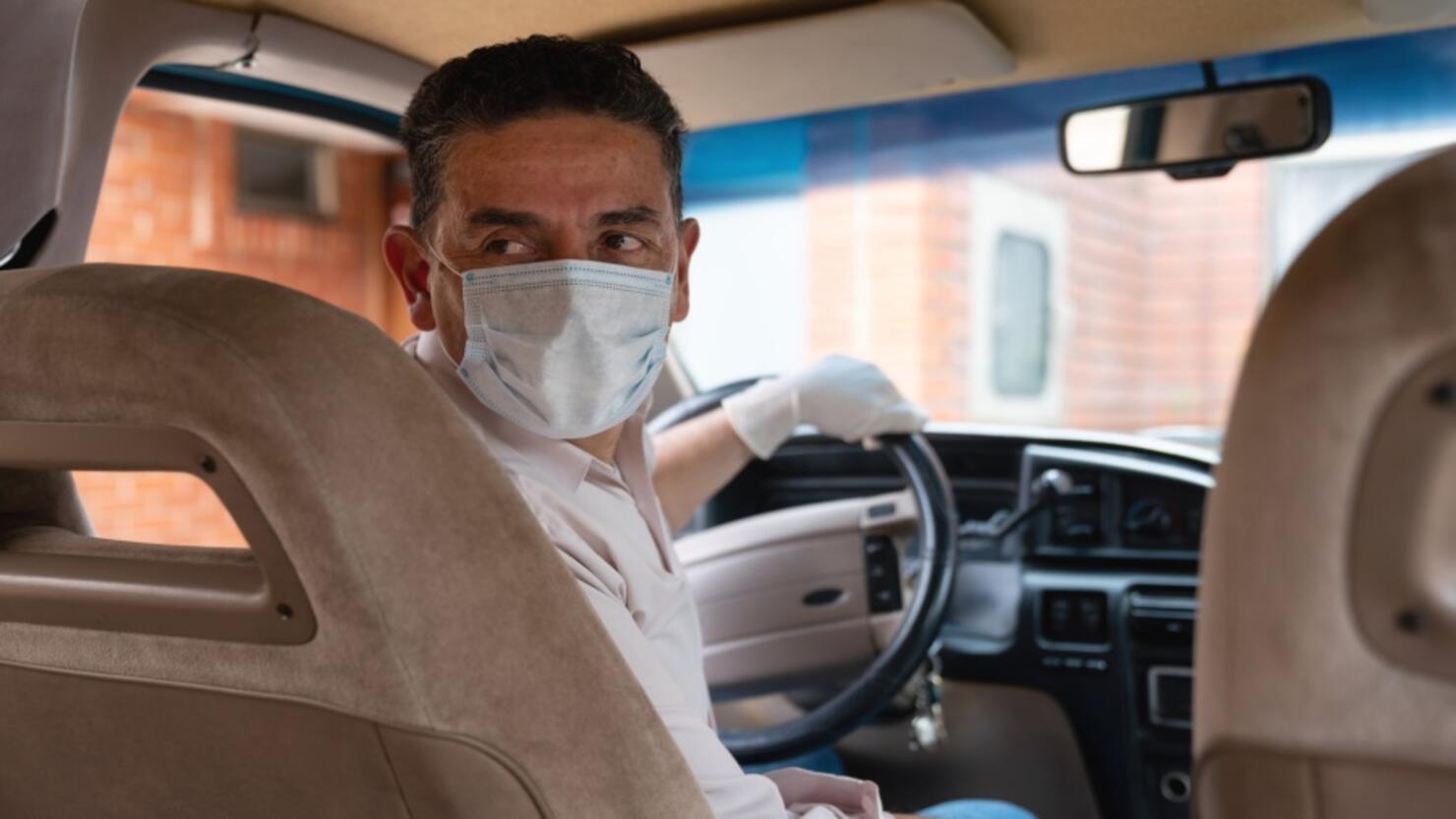 Driver wearing a facemask and gloves in his car