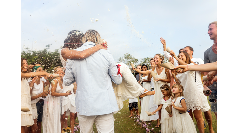 Wedding guests tossing rice at newlyweds, outdoors