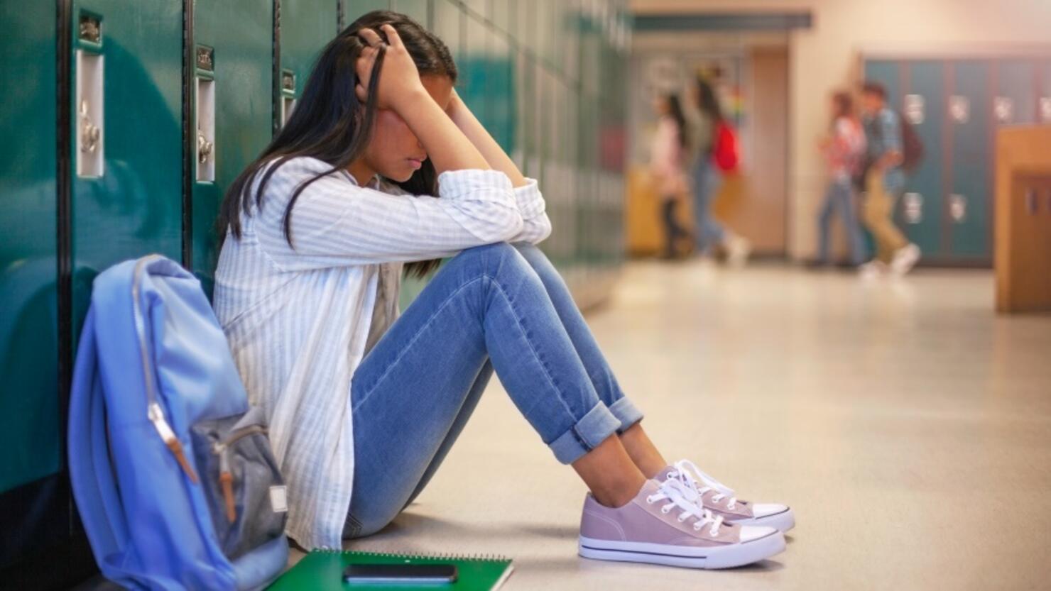 Frustrated Asian teenage young woman female student with head in hands in hallway in school