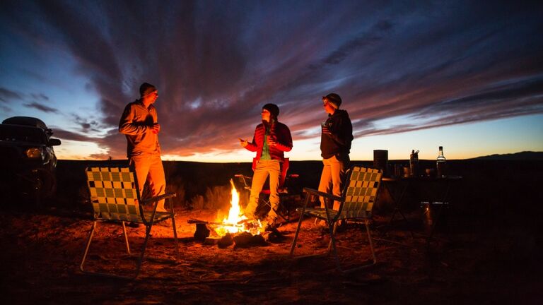 Three friends handing out at a campfire.