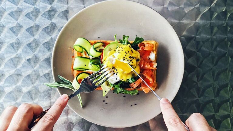 Eating brunch with waffle, avocado, cucumber, salmon and poached egg, personal perspective