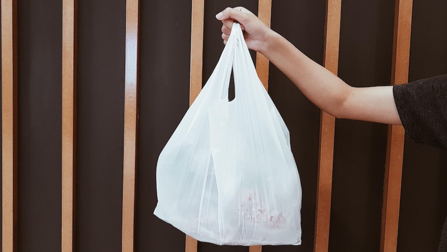 Cropped Hand Holding Plastic Bag Against Metal Grate