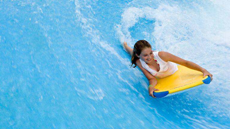Girl (11-13) riding body board in water park