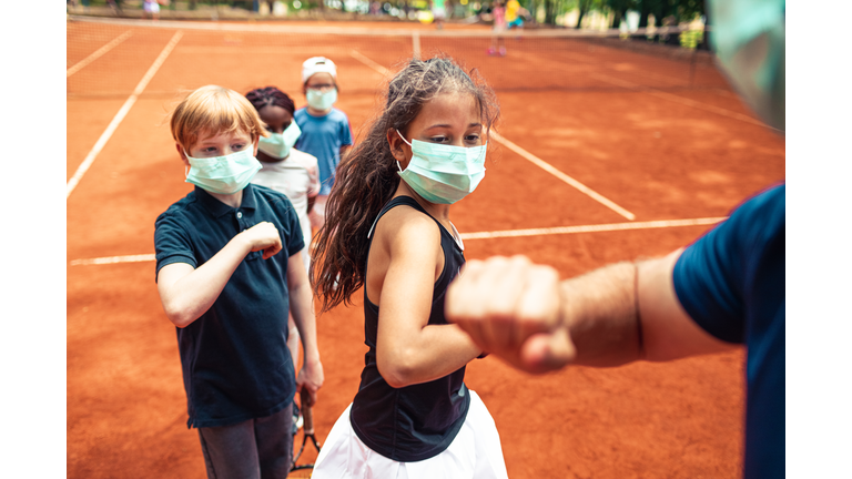 Kids elbow bumping their tennis instructor