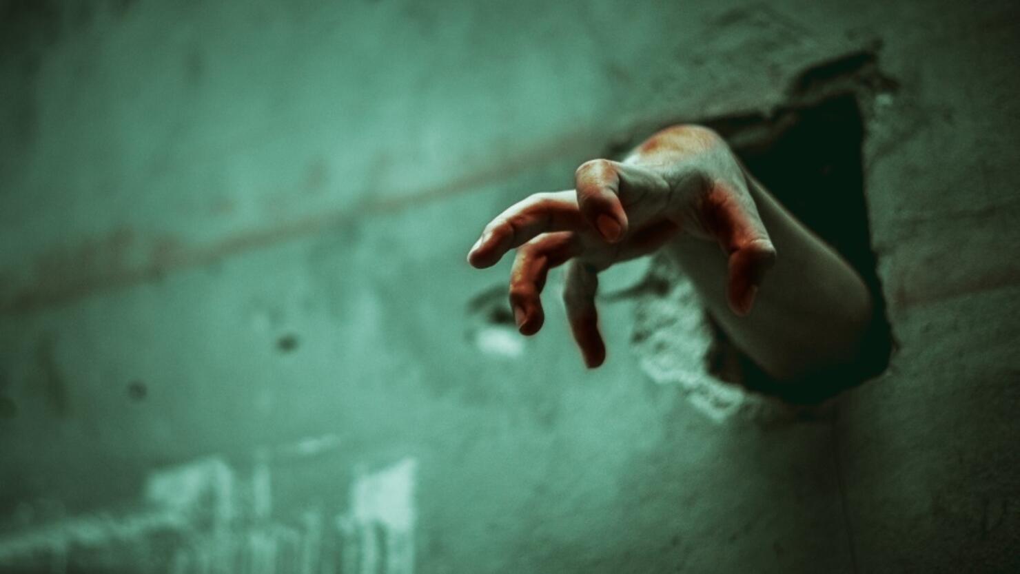 Zombie hand through the cracked wall. Horror and scary film concept. Halloween day theme. Green tone like ghost movie