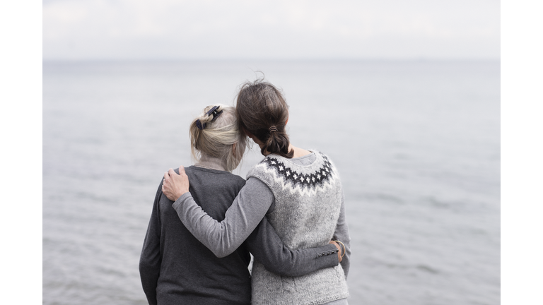 two generations women embracing, looking at sea