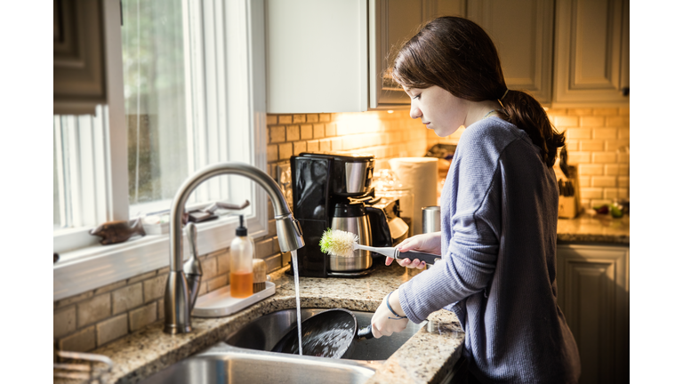 Teenage girl doing dishes in kitchen