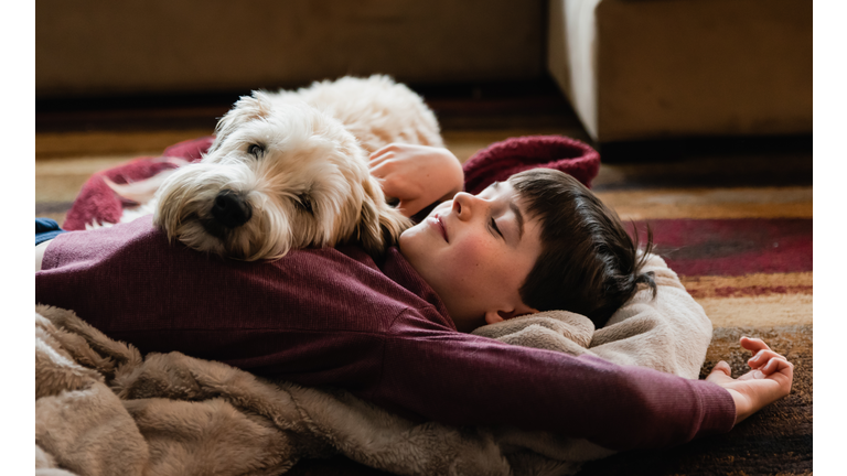 Boy and his dog cuddling on the floor together on a blanket.