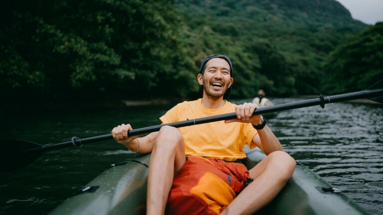 Man paddling kayak in mangrove river and laughing, Iriomote, Japan