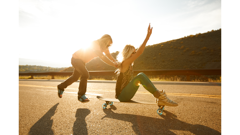 A guy pushing a girl on a skateboard.