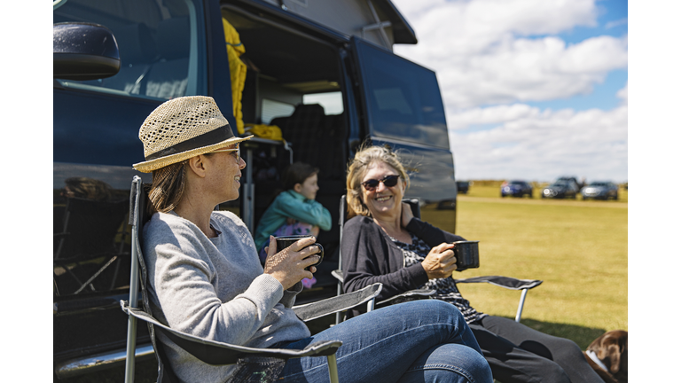 Woman having a cuppa by the camper van with her mother and daughter