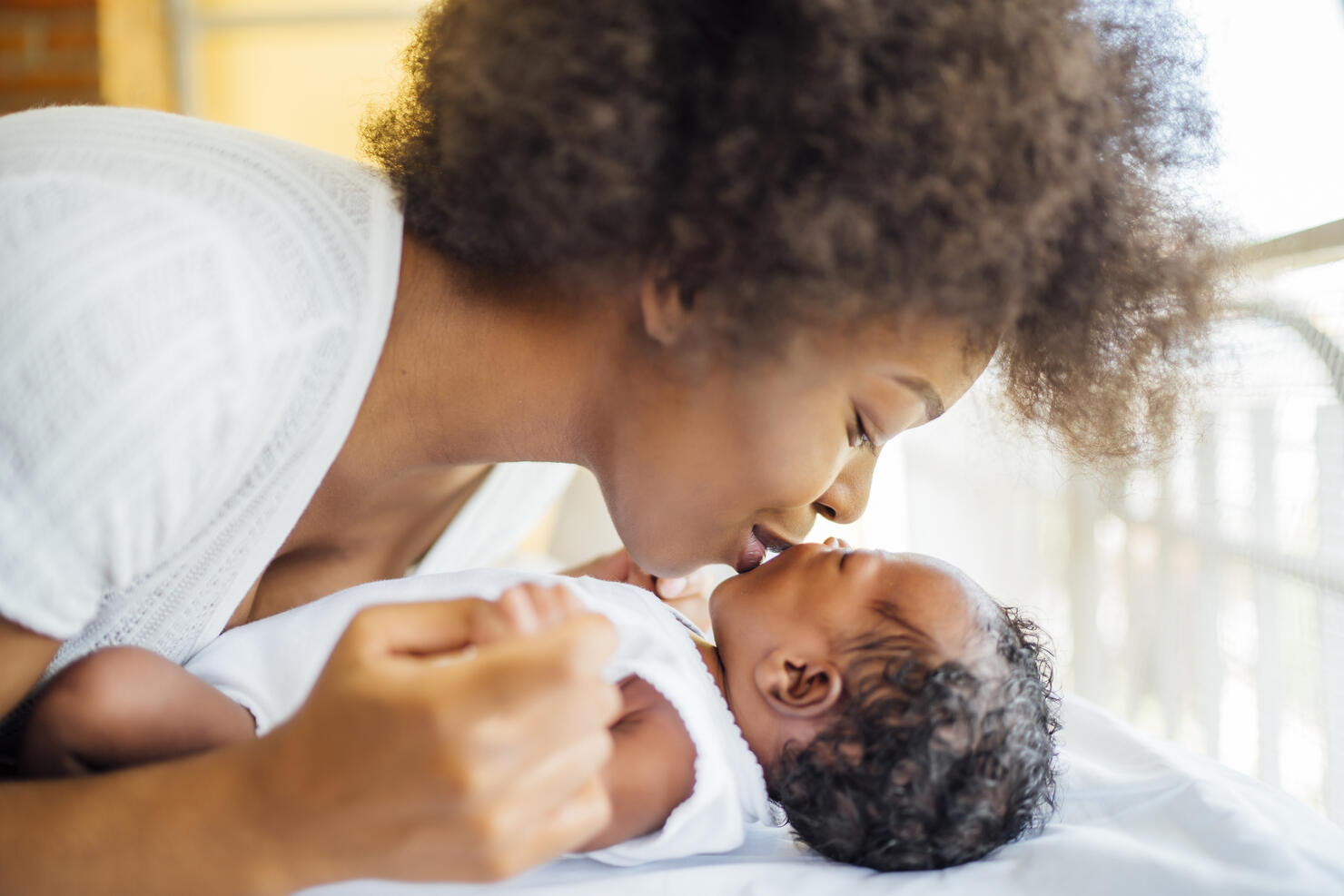 Close-up of mother kissing baby daughter lying on bed at home