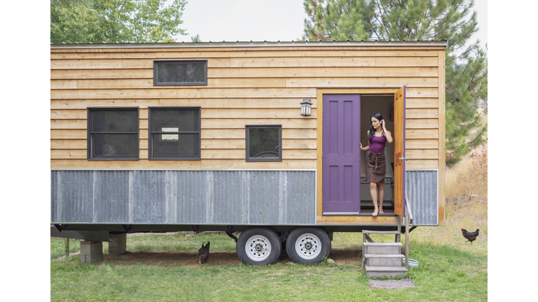 Young woman looking out door of her tiny house