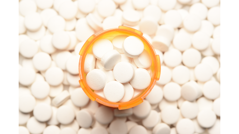 Prescription bottled filled with pills surrounded by more of the same tablets