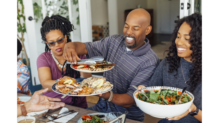 Smiling man serving food to family during outdoor dinner party