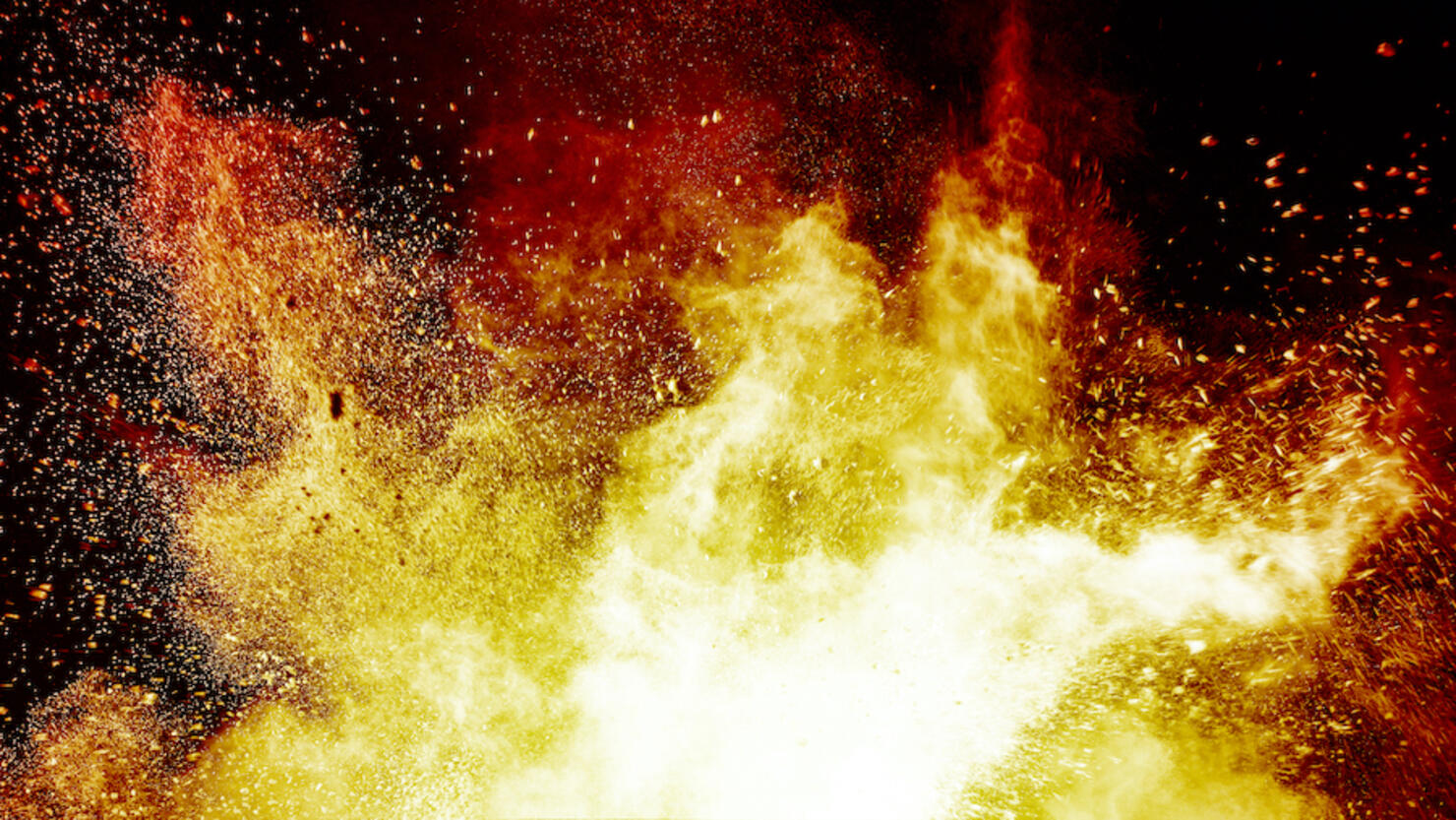 Explosion by an impact of a cloud of particles of powder and smoke of color orange and yellow on a black background.