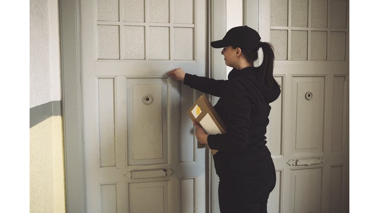 Side view of delivery woman with package knocking at door