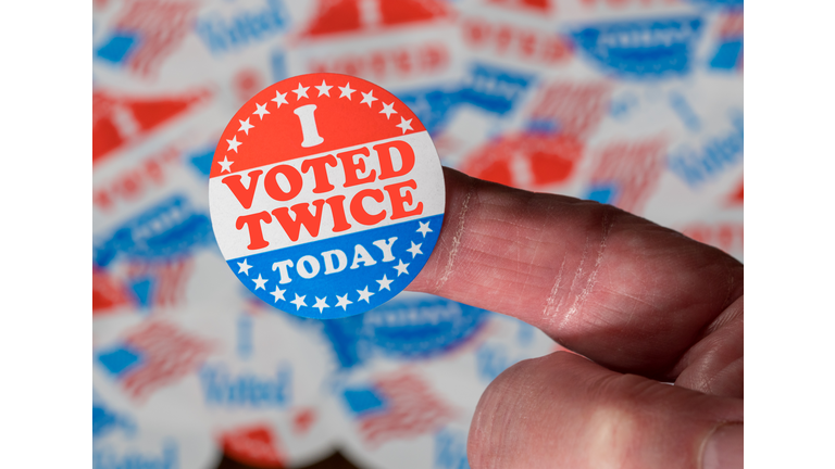 Finger with I Voted Twice sticker in front of many election voting badges to illustrate voter fraud