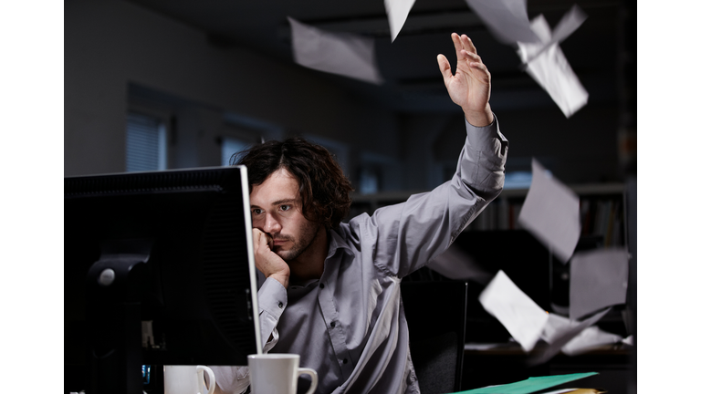 Office worker working late, throwing paper in the air