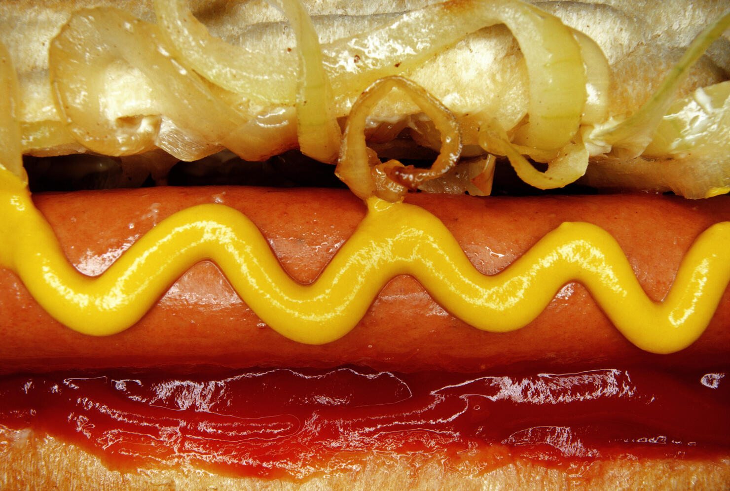 Hotdog with mustard, tomato ketchup and onions, close-up